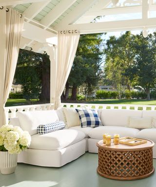 Outdoor terrace with bench seating, round coffee table, potted flowers, white curtains
