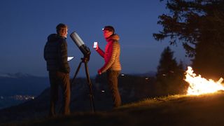 Two men using the Unistellar eVscope 2 outside at night