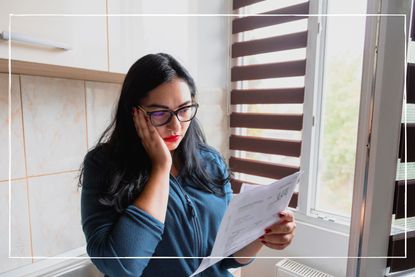 worried woman looking at her energy bill by an open window at home