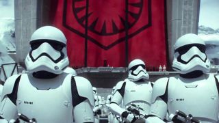 Still from a Star Wars movie. Here we see a whole army of gleaming white storm troopers standing in formation in front of a giant red banner.