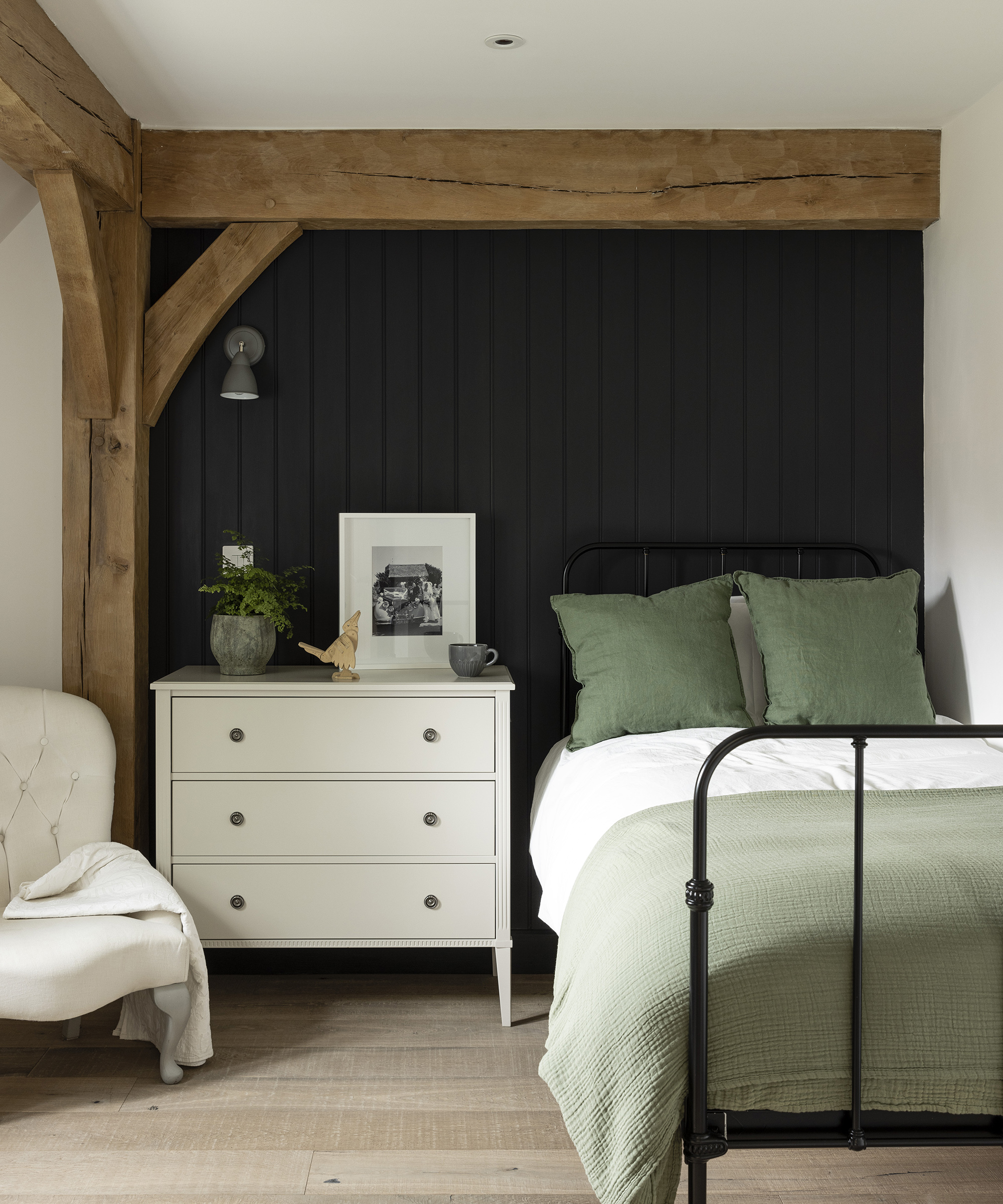 A single bedroom with iron frame bed and dark wooden panelling on the wall