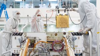 People in clean room white suits lowering a golden box into Perserverance.