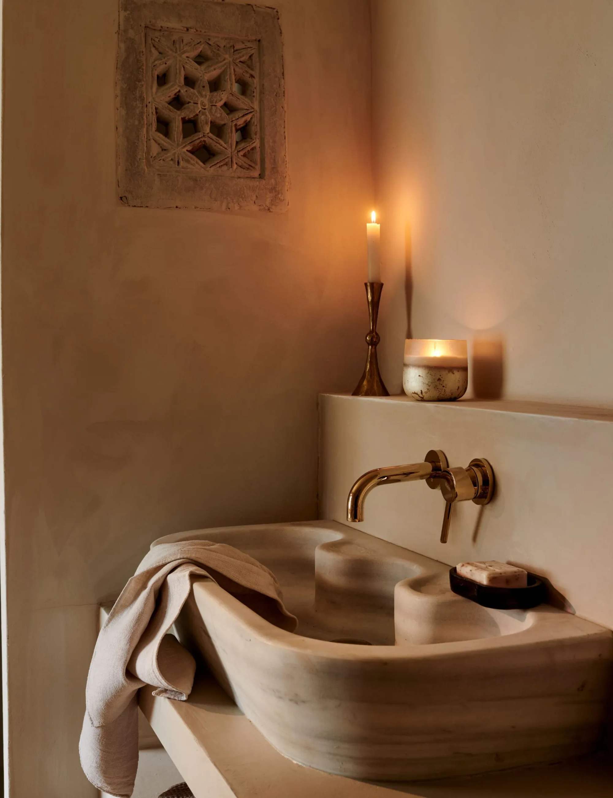 A carved stone sink in a plaster-wall bathroom. A candle lit on the ledge above.