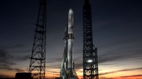 A white rocket stands against a setting sunet-painted sky.
