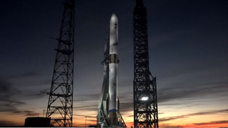 A white rocket stands against a setting sunet-painted sky.