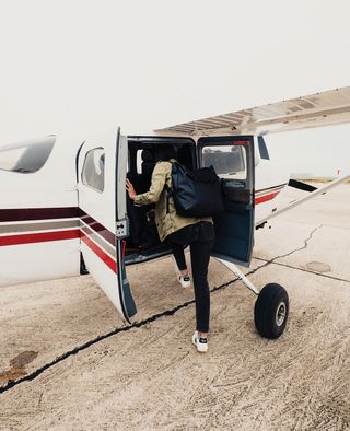 A woman wearing black jeans getting into the back of a small plane.
