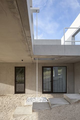 The outside area is covered with sand. There are steps that lead to the second floor, and a white chain that serves as a rainwater drain.