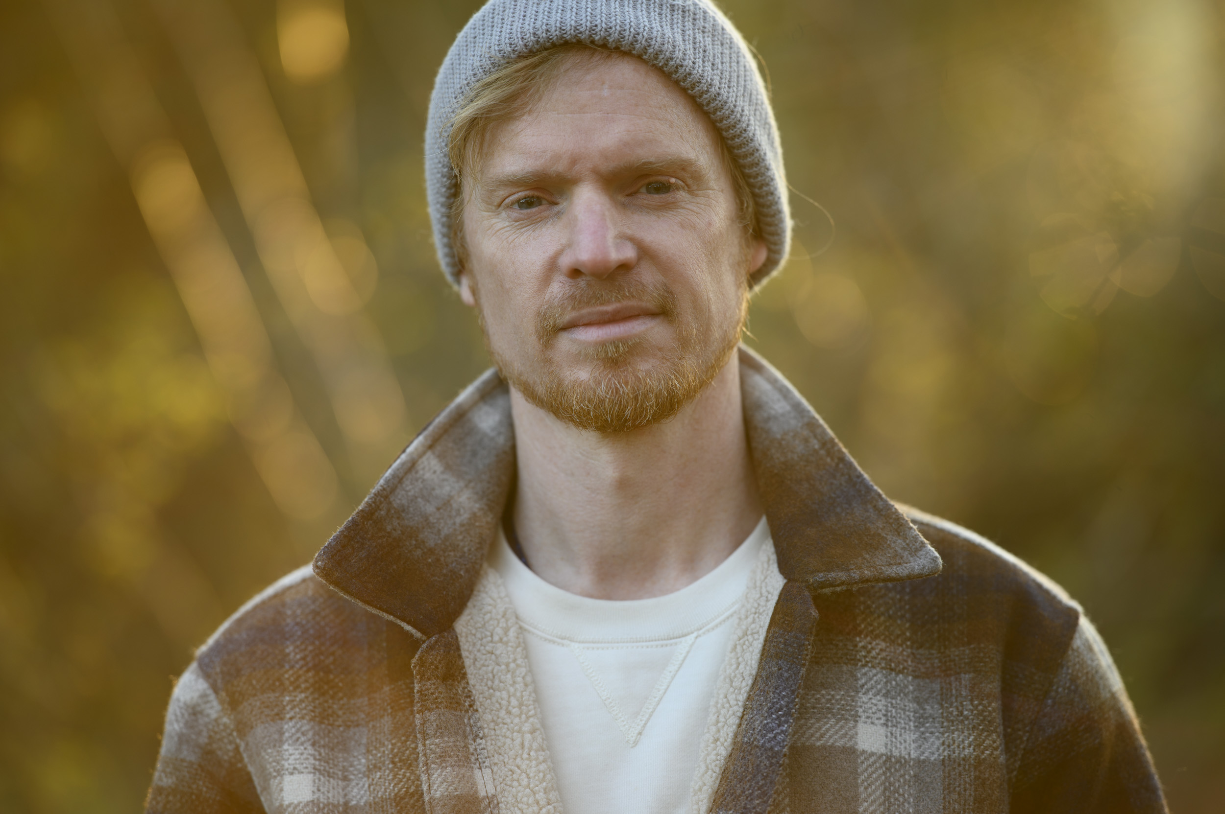 Portraits of a man in a beanie hat and shacket and golden hour with dappled light in background