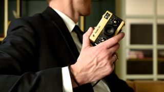 Rollei 35 Retrospekt 24K Gold Edition camera being held by a suited person wearing gold rings