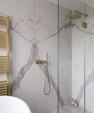 Marbled shower with clear glass shower doors and gold-plated shower head and towel rack