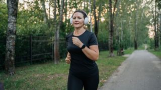 Woman running early in the morning along park towpath with headphones on