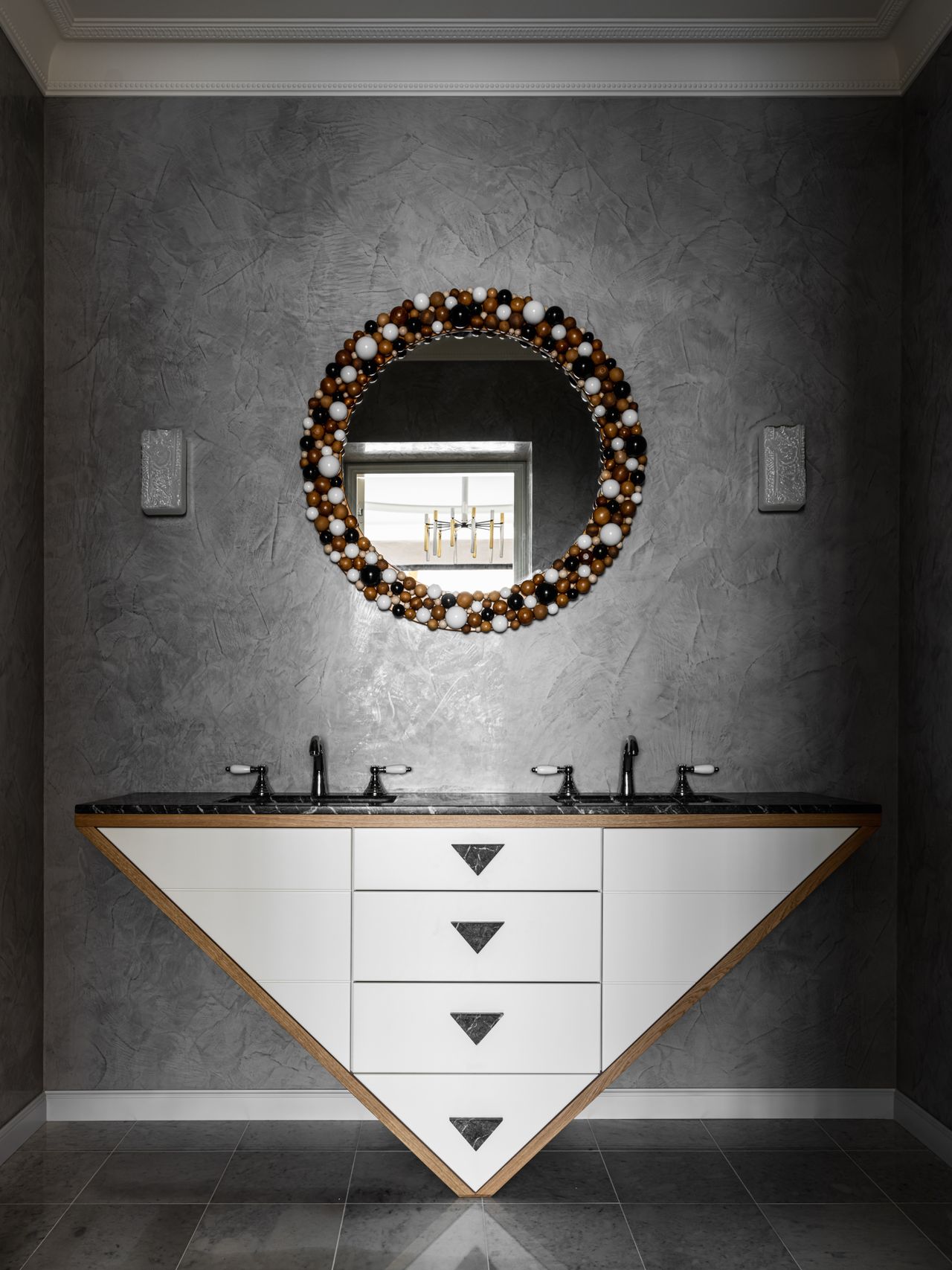 A bathroom with dark-toned walls and floor, and a round mirror