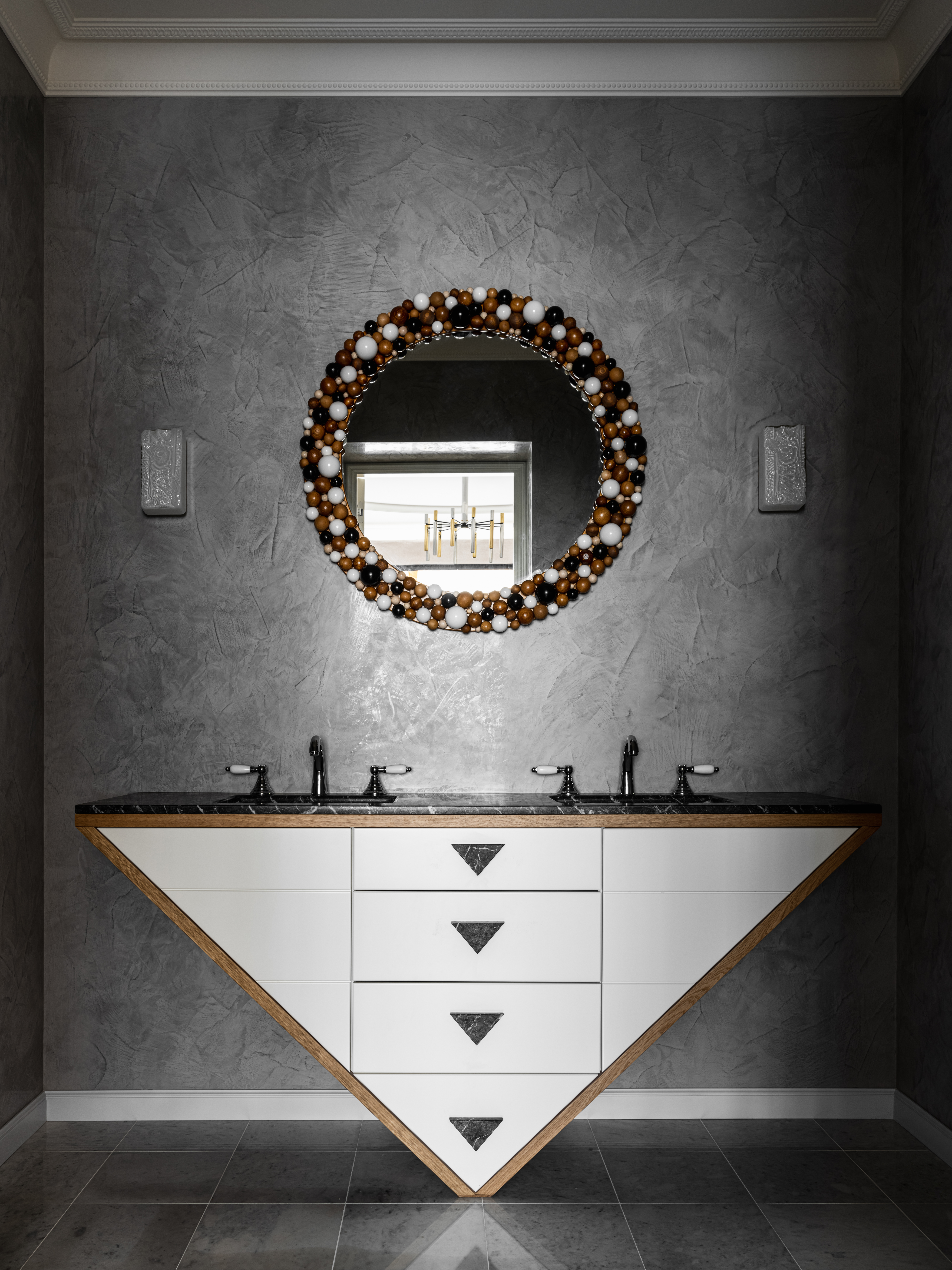 A bathroom with dark-toned walls and floor, and a round mirror