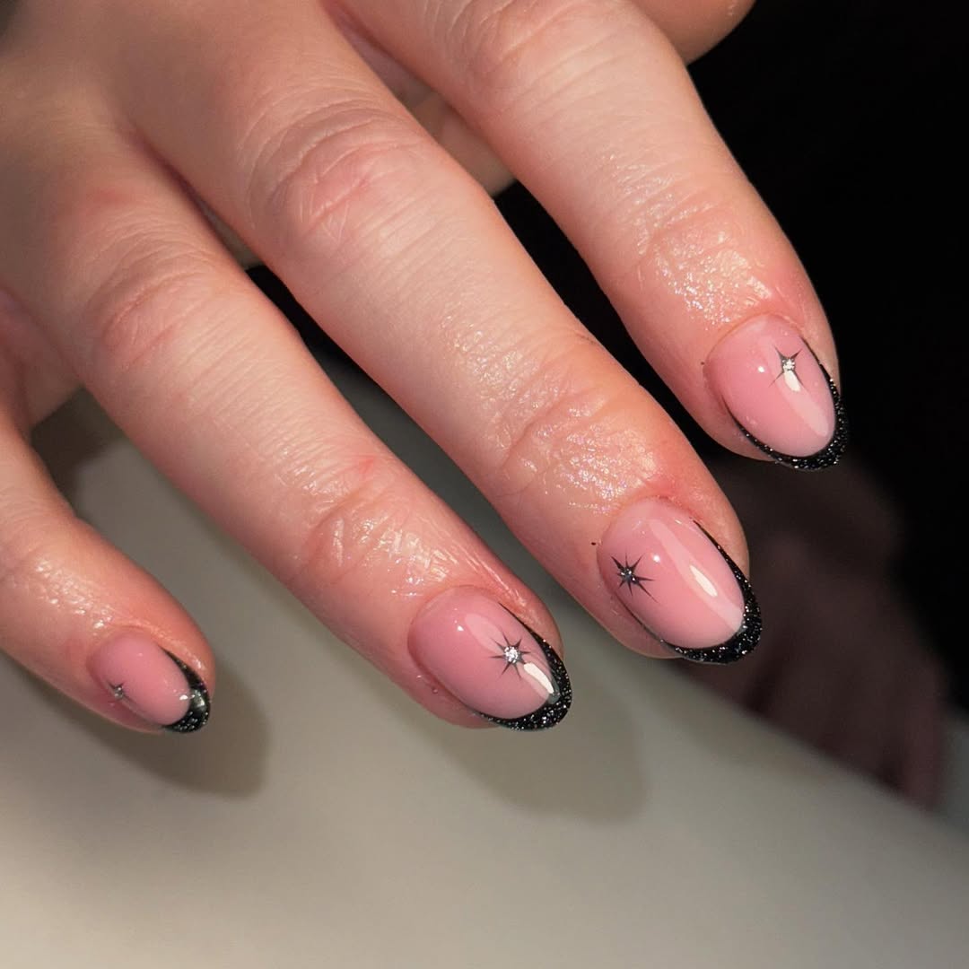 a person wearing a black french manicure with star designs and silver glitter