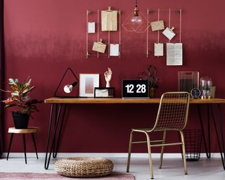 Home office with dark red walls, desk with industrial pin legs, and a metal chair with no cushioning