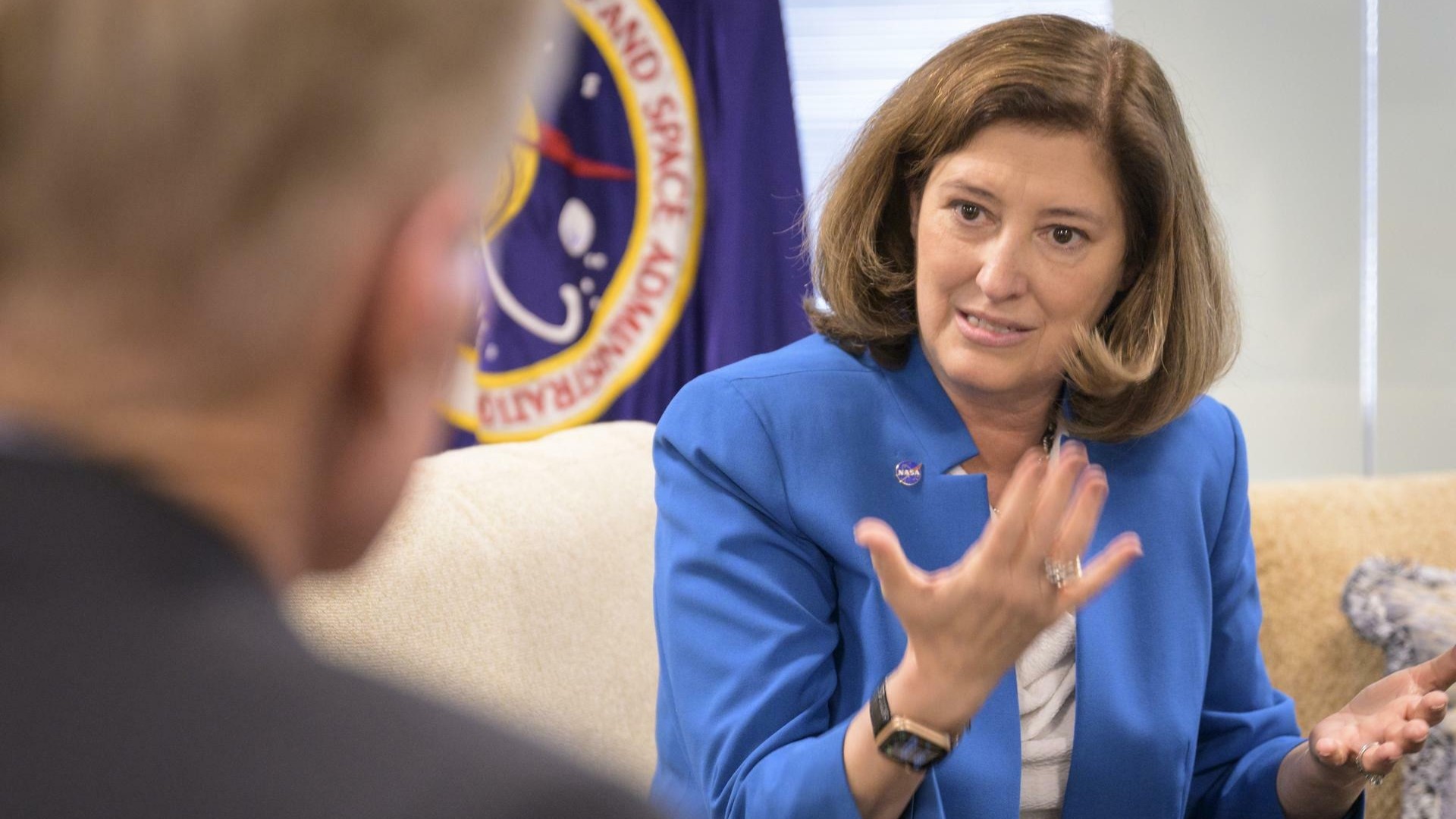 A woman in a blue jacket gestures with her hands.
