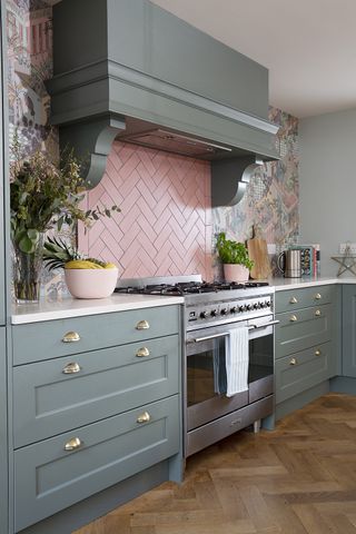 Portrait shot of green kitchen with a pink tiled splashback and patterned wallpaper