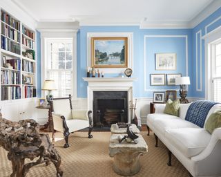 A library with light blue walls, marble fireplace and a bookcase wall