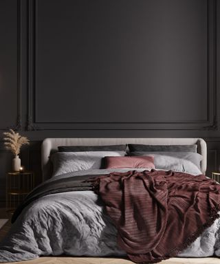 A black bedroom with black wall and, a gray bed with burgundy and gray bedding