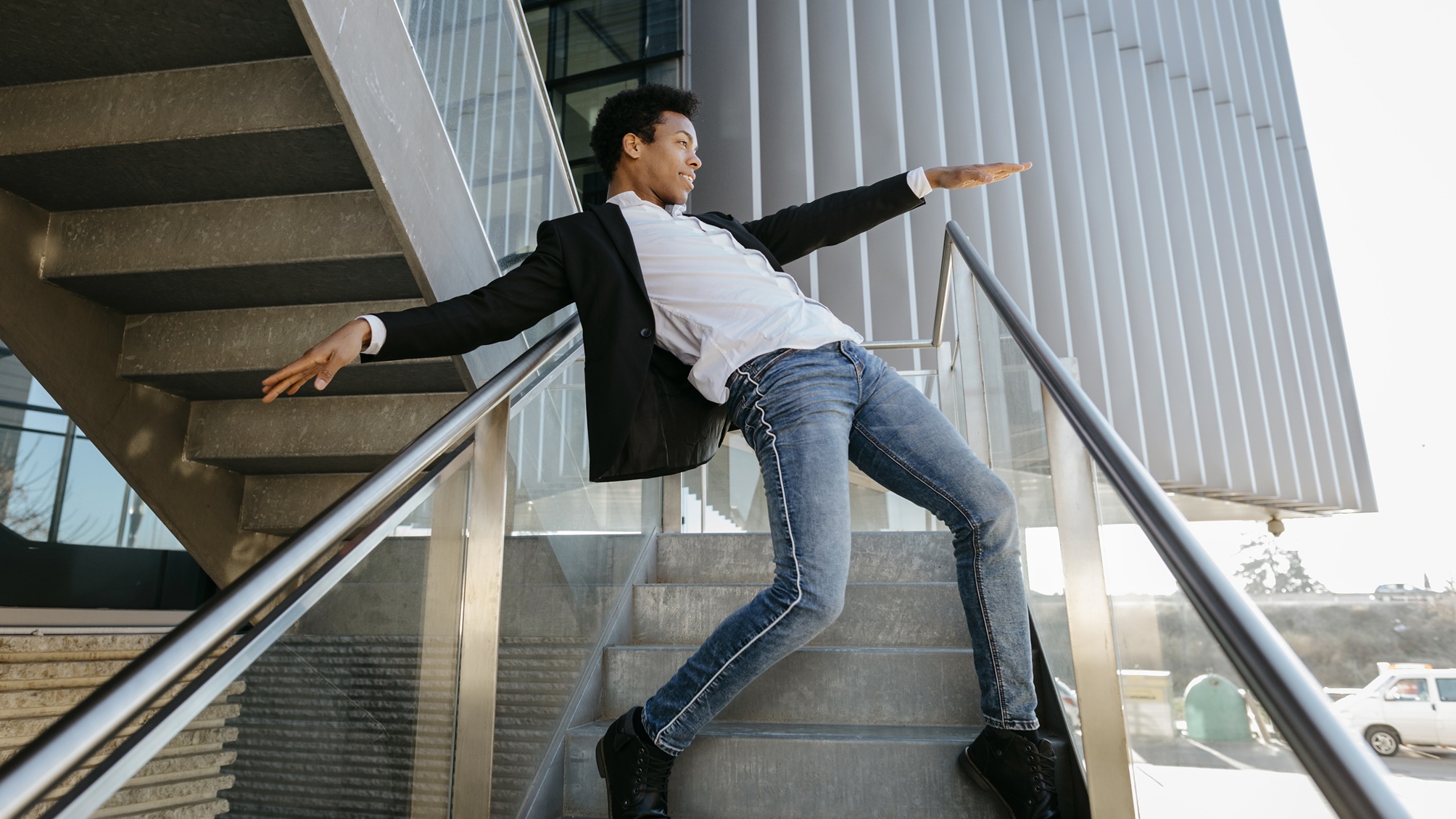 A young man appears to be dancing on a staircase with railings on either side of him.