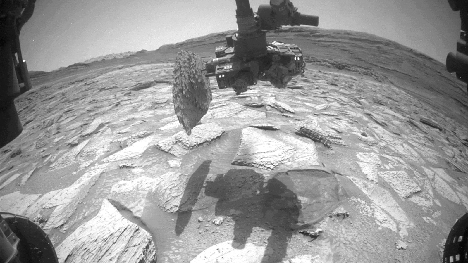 A black and white photo showing the rock stuck to the drill of Curiosity's robot arm