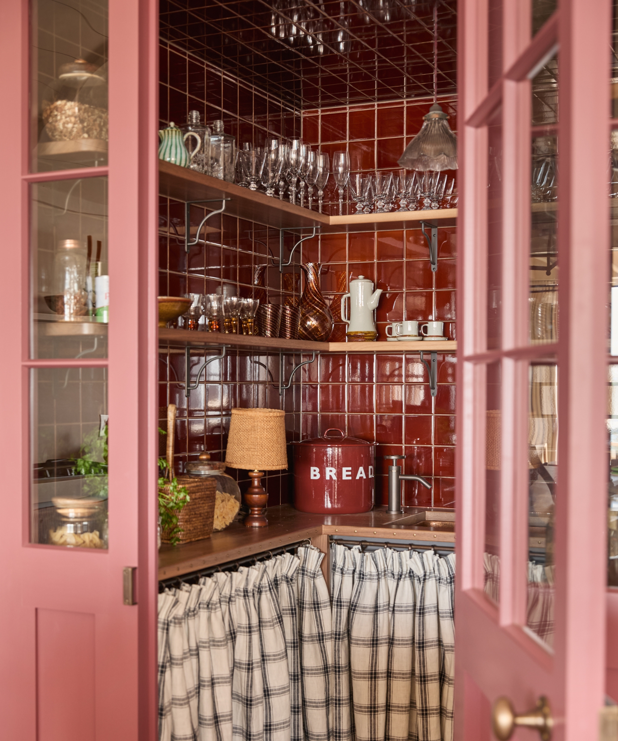 A small walk-in pantry with oxblood red tiles, wooden shelving and countertops, and a white and green checkered cabinet skirt