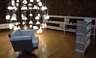 Gloss wooden floor, brick walls, grey armchair, large light display with white shades, low shelving units in grey to the right and back wall