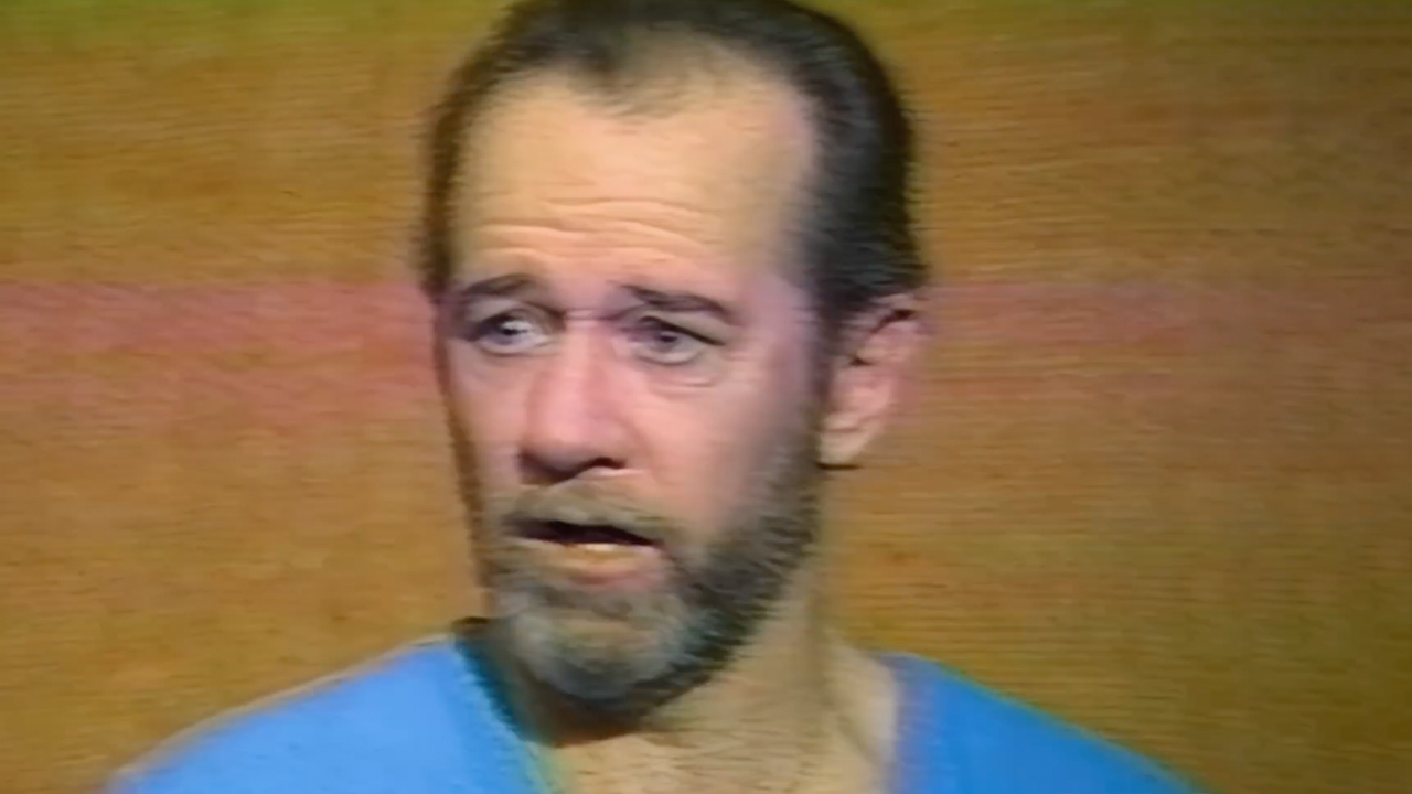 Archival interview footage of George Carlin, wearing a blue shirt and looking serious, footage featured in HBO's doc George Carlin American Dream.