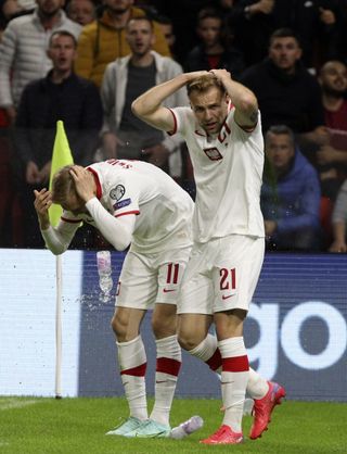 Poland’s Karol Swiderski, left, holds his head as fans throw missiles onto the pitch following his goal