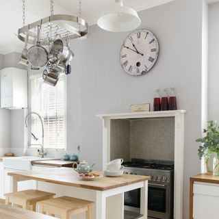 White kitchen with small kitchen island with wood worktop and pans hung from a rack suspended from the ceiling