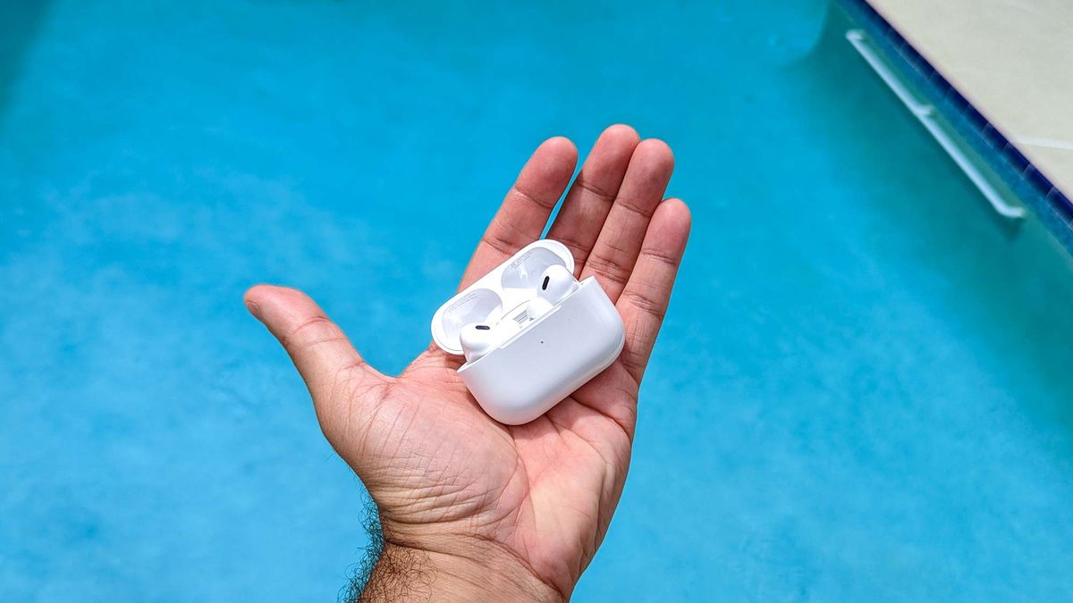 Apple AirPods Pro in charging case in palm of reviewer&#039;s hand with pool in the background