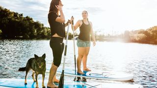 Two women paddle boarding with their dog