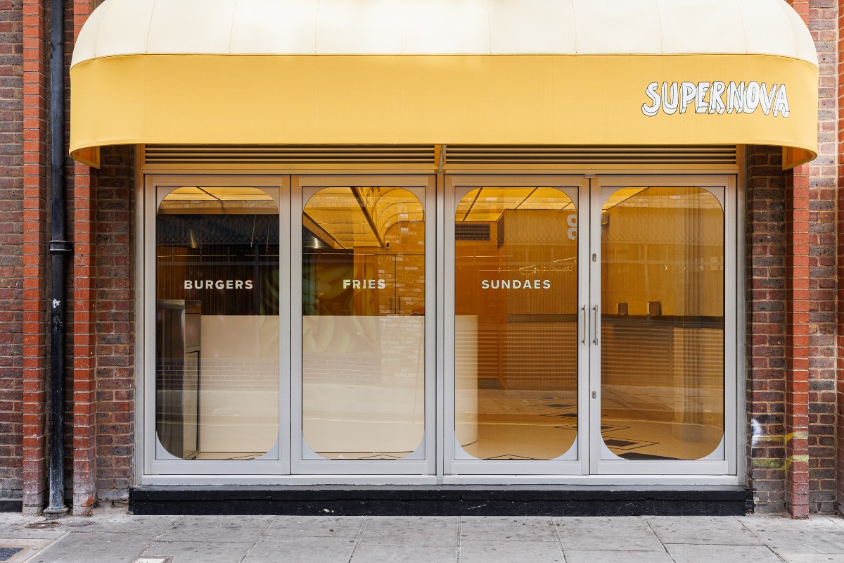 A yellow-tinted burger chain&#039;s shop front features a slightly spaceship-like look, with oblong windows, plump akwinings, red brick walls, and a warm atmosphere inside.