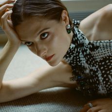 Photo of Louisa Jacobson laying down with her right hand resting on her head. She is wearing a scarf-print Dries van Noten halter dress. 