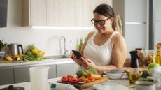 Woman leaning on kitchen counter looking at a smartphone