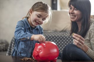 Mother with daughter putting coins into a red pig money box
