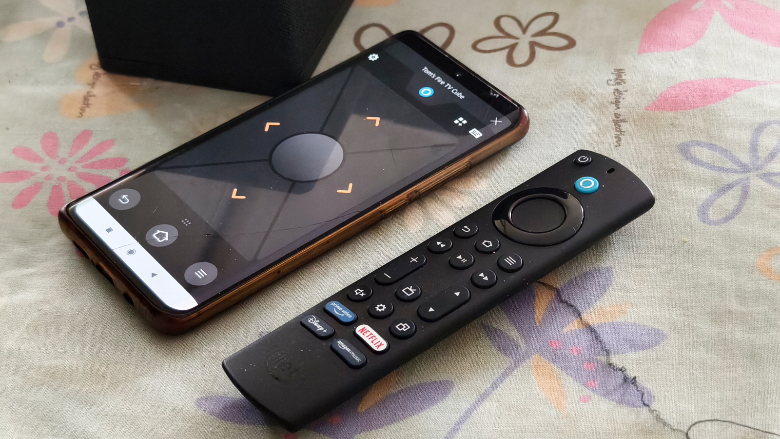A smartphone with the Amazon Fire TV app next to the Alexa remote
