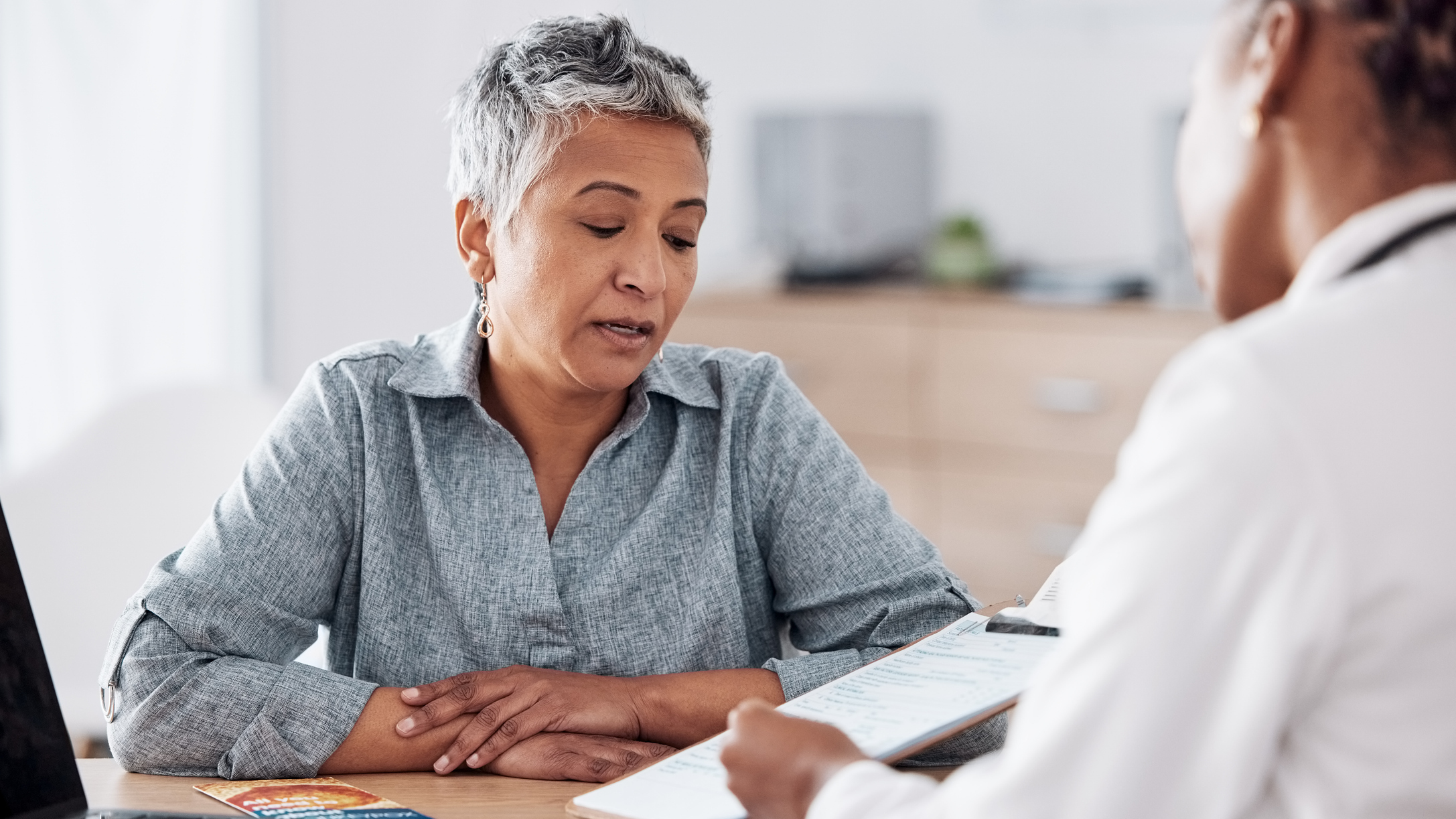 Woman looks at clipboard in conversation with person in a white shirt 