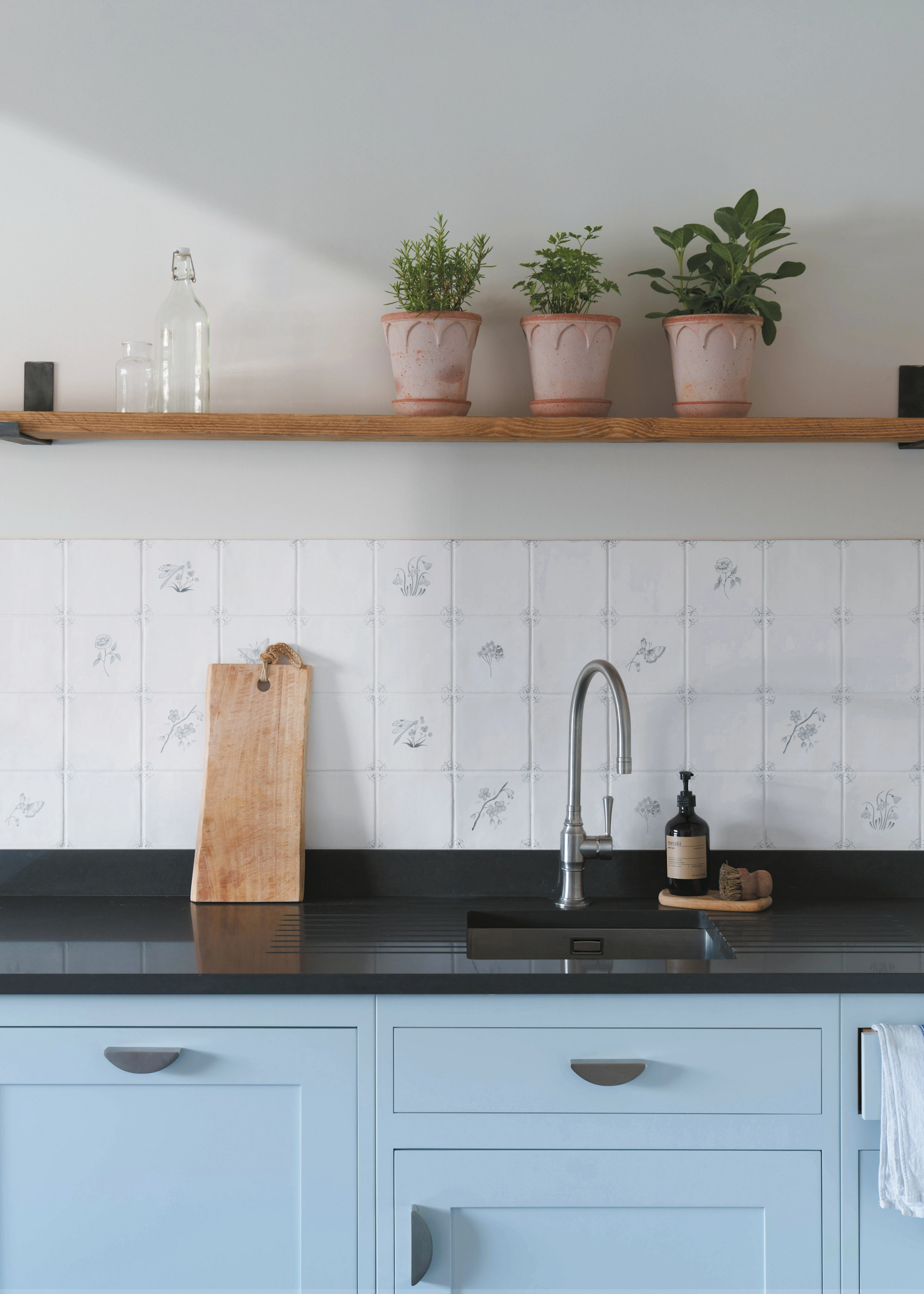 a pale blue kitchen with dark worktops and vintage style tiles for the backsplash