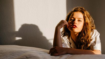 girl leaning against a bed with wavy hair