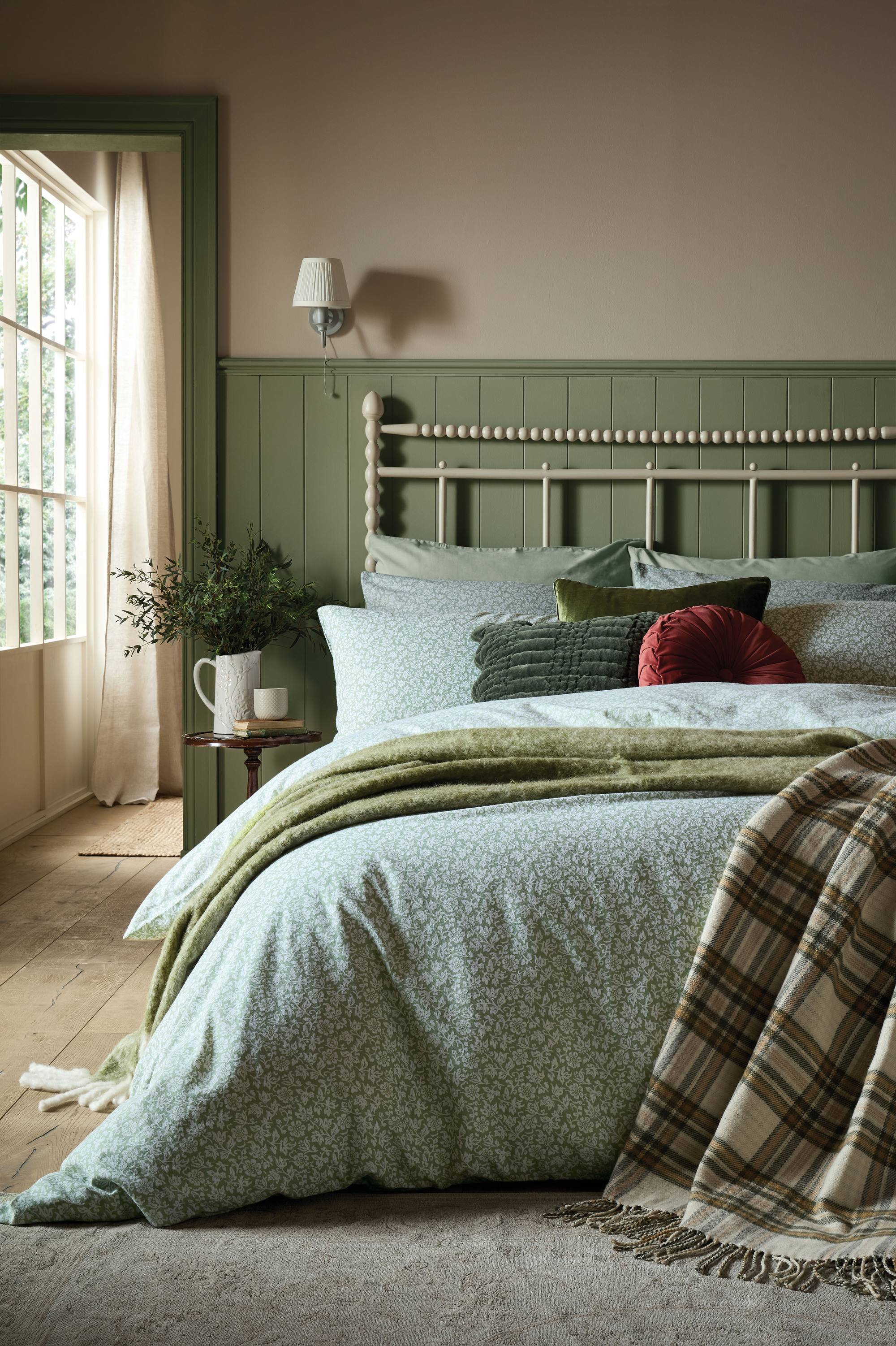 A bedroom with sage green panelling, a cream iron bedframe, and blue and green bedding