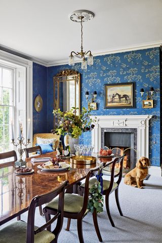 dining room with traditional wooden chairs and table with blue patterned wallpaper and origianl firplace