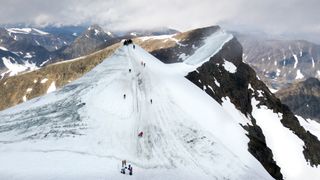 Drone photo of people walking up to the southern peak of Kebnekaise, the highest mountain in Sweden. Behind the northern peak is visible.