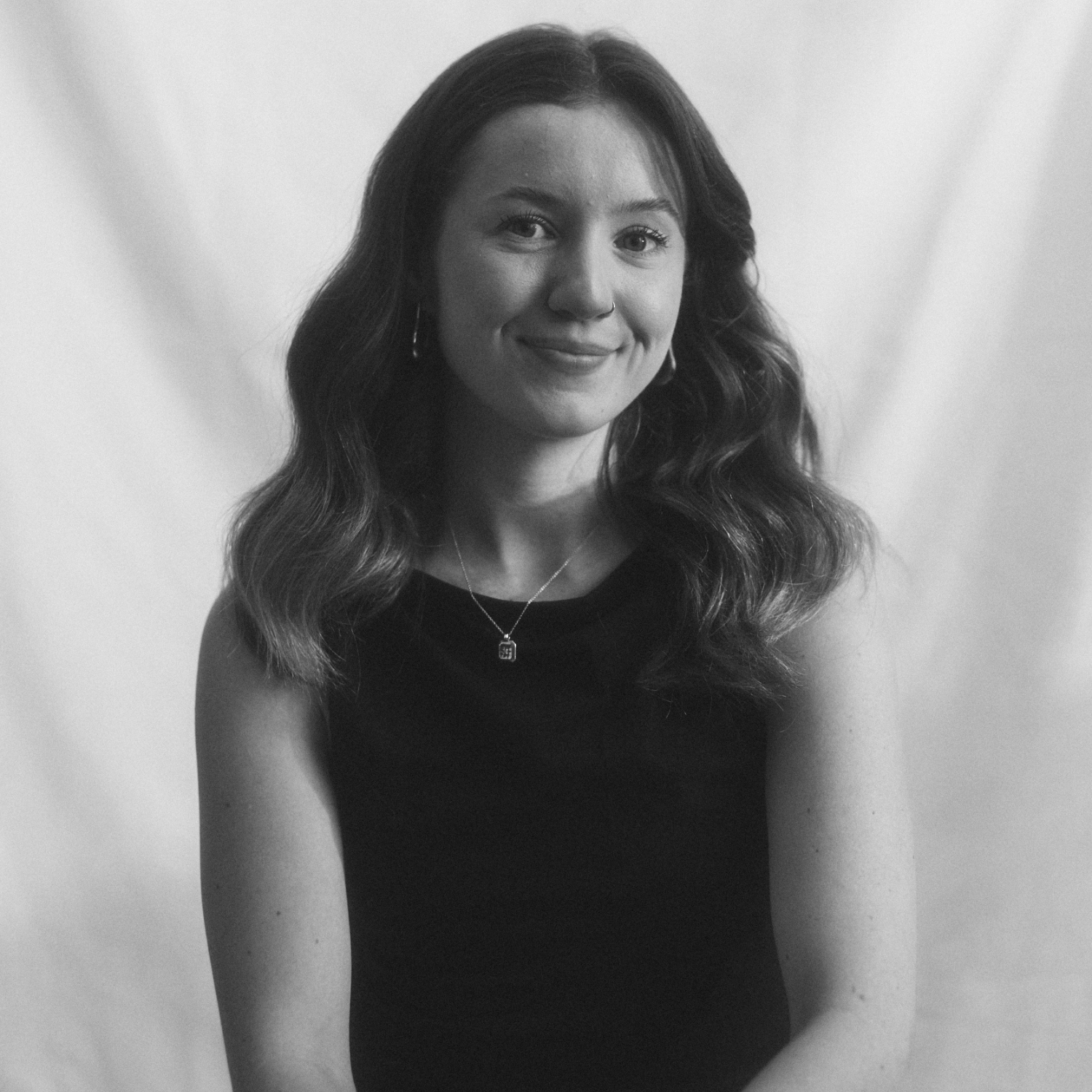 A black and white headshot of a girl with wavy hair, in a black sleeveless top