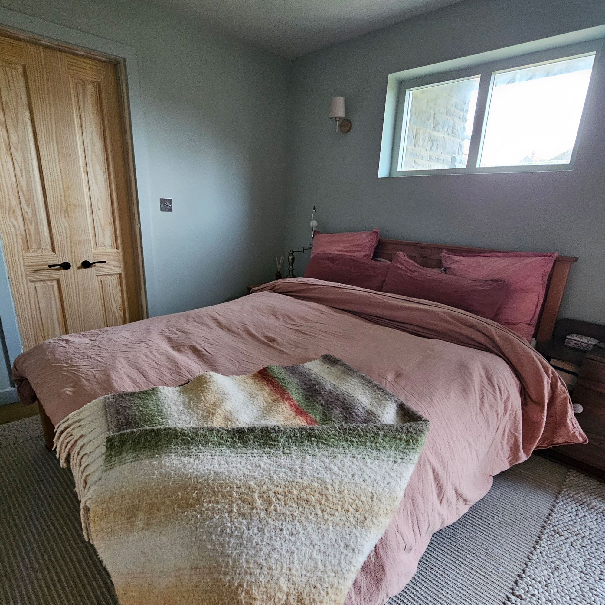 Blue bedroom with pink, red and purple bedding and a woollen throw