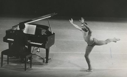 man dancing on one leg next to a piano