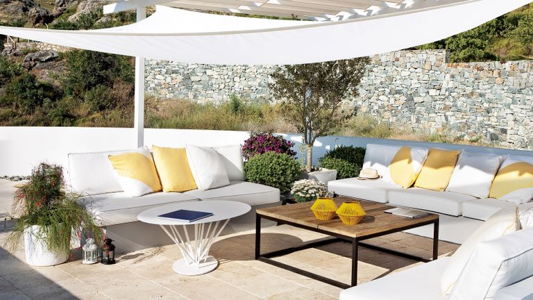 A white shade sail over a contemporary outdoor sofa with coffee tables