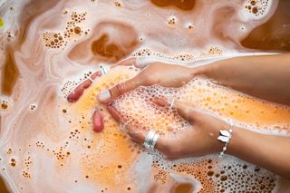 A person's hands in a bath with an orange dissolved bath bomb.