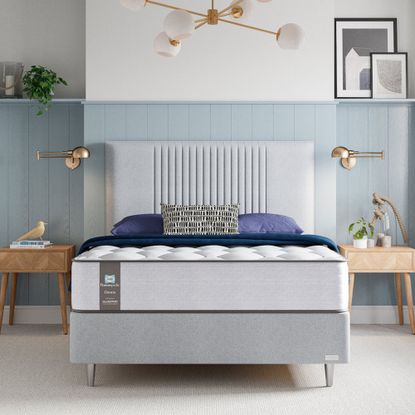 The Sealy Newton Posturepedic Mattress on a grey upholstered bedrame in a bedroom with pale blue panelled walls