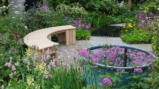 raised circular water feature and curved wooden garden bench surrounded by colourful flowers and planting